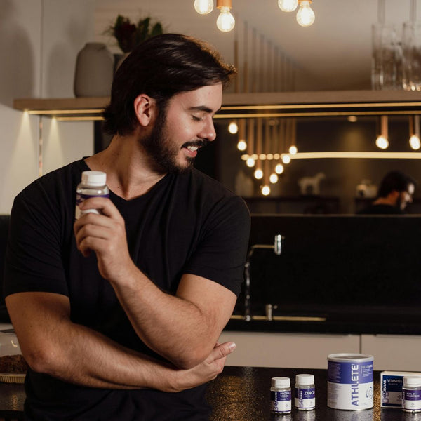 Man holding a supplement bottle in a kitchen setting