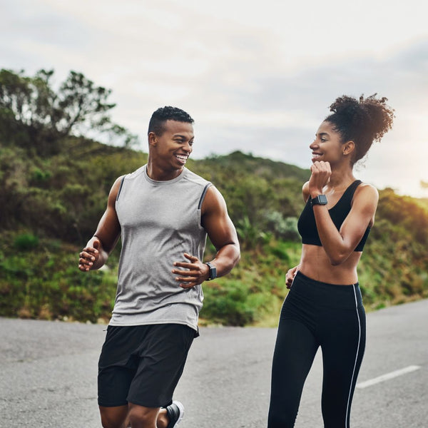 Two people jogging outdoors on a road with greenery in the background