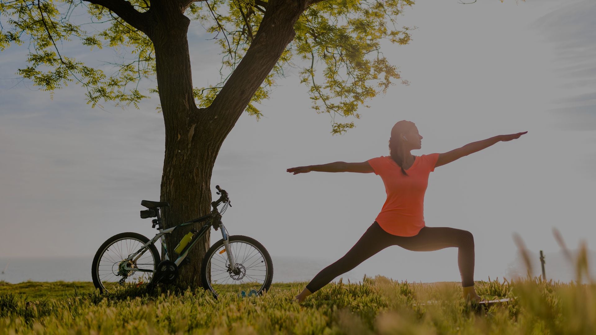 Person practicing yoga in a field with a bicycle leaning against a tree